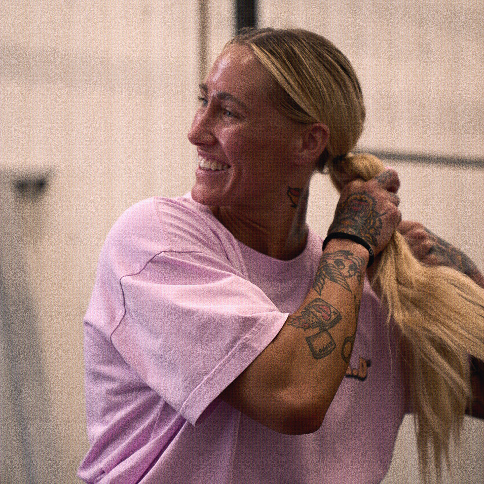 Woman with tattoos holding blonde hair wearing DBE Crop Tee Soft Purple